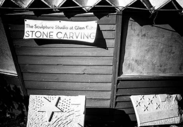 Black & white photo of the outside of the wooden Sculpture Studio with the words Sculpture Studio on a white sign