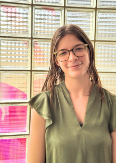 Staff portrait of young adult female with brown hair and glasses wearing a light green short sleeve top.